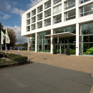 Parkplatz vor dem ATLANTIC Hotel Galopprennbahn in Bremen Eingangsbereich des ATLANTIC Hotels mit moderner Glasfassade, davor Parkplätze und Fahnen.