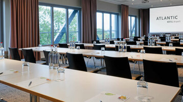 ATLANTIC Hotel Airport Tagen Moderner Konferenzraum im ATLANTIC Hotel Airport Bremen mit Tischen, Stühlen und großer Leinwand.