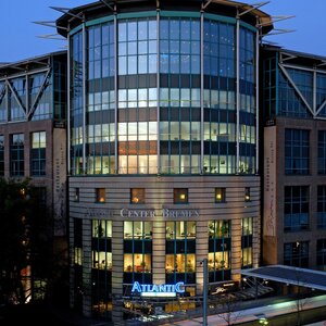 Außenansicht des ATLANTIC Hotel Airport in Bremen bei Dämmerung Modernes Gebäude des ATLANTIC Hotel Airport Bremen bei Dämmerung, mit beleuchteter Glasfassade und vorbeifahrender Straßenbahn.