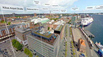 Aeromovie | Drohnenflug ATLANTIC Hotel Kiel Luftaufnahme des ATLANTIC Hotel Kiel, umgeben von Stadtgebäuden und dem Hafen mit Fähren am Ostseekai.
