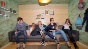 Jugendliche auf einem Sofa zur Aktion "Frühstücksspecial" des ATLANTIC Hotel Universum Bremen Fünf Personen sitzen fröhlich auf einem Sofa in einem bunt dekorierten Raum.