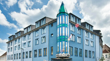 ATLANTIC Hotel Vegesack Bremen Außenansicht des ATLANTIC Hotel Vegesack in Bremen mit blauer Fassade und markantem Glasturm bei Tageslicht.