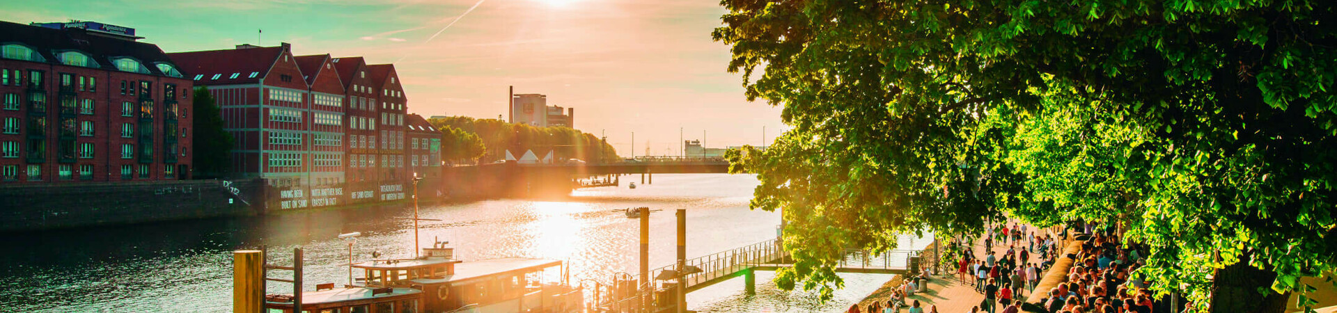 Bremer Schlachte im Frühling Sonnenuntergang an der Weserpromenade in Bremen mit Menschen, Booten und historischen Gebäuden im Hintergrund.