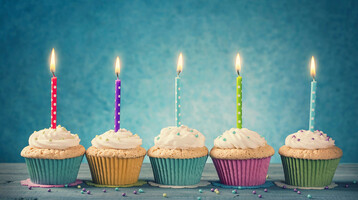 Cupcakes mit Kerzen Fünf bunte Cupcakes mit brennenden Kerzen auf blauem Hintergrund.
