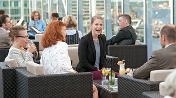 Gäste in der Bar Deck 8 des ATLANTIC Hotel Kiel Personen genießen Getränke auf einer modernen Hotel-Dachterrasse mit Blick auf die Stadt.