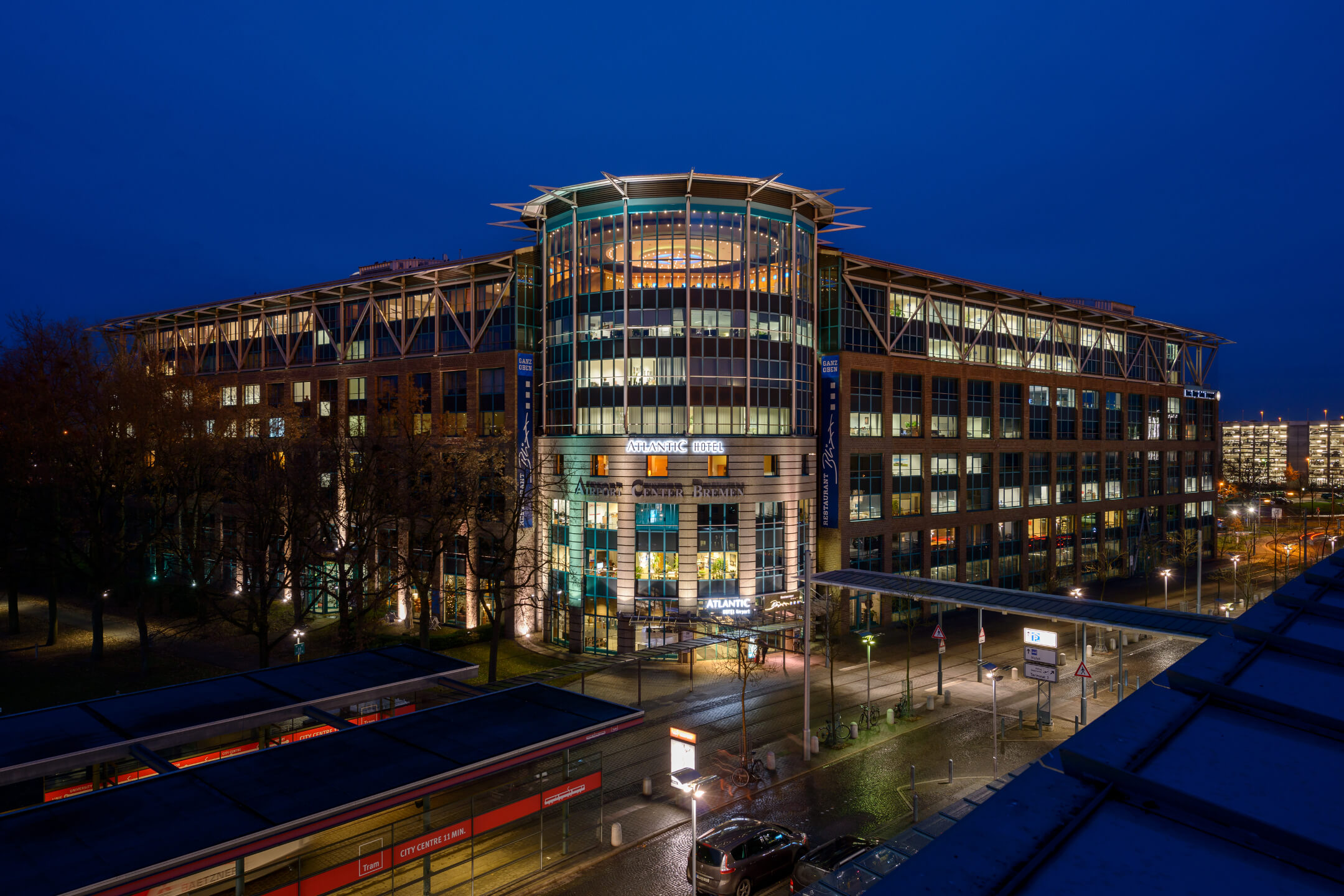 ATLANTIC Hotel Airport bei Nacht, modernes Gebäude mit beleuchteten Fenstern und Eingangsbereich, blauer Himmel.