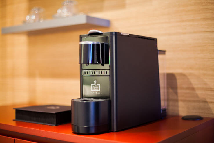 Kaffeemaschine auf rotem Tisch im ATLANTIC Hotel Airport Bremen, mit Gläsern im Hintergrund.