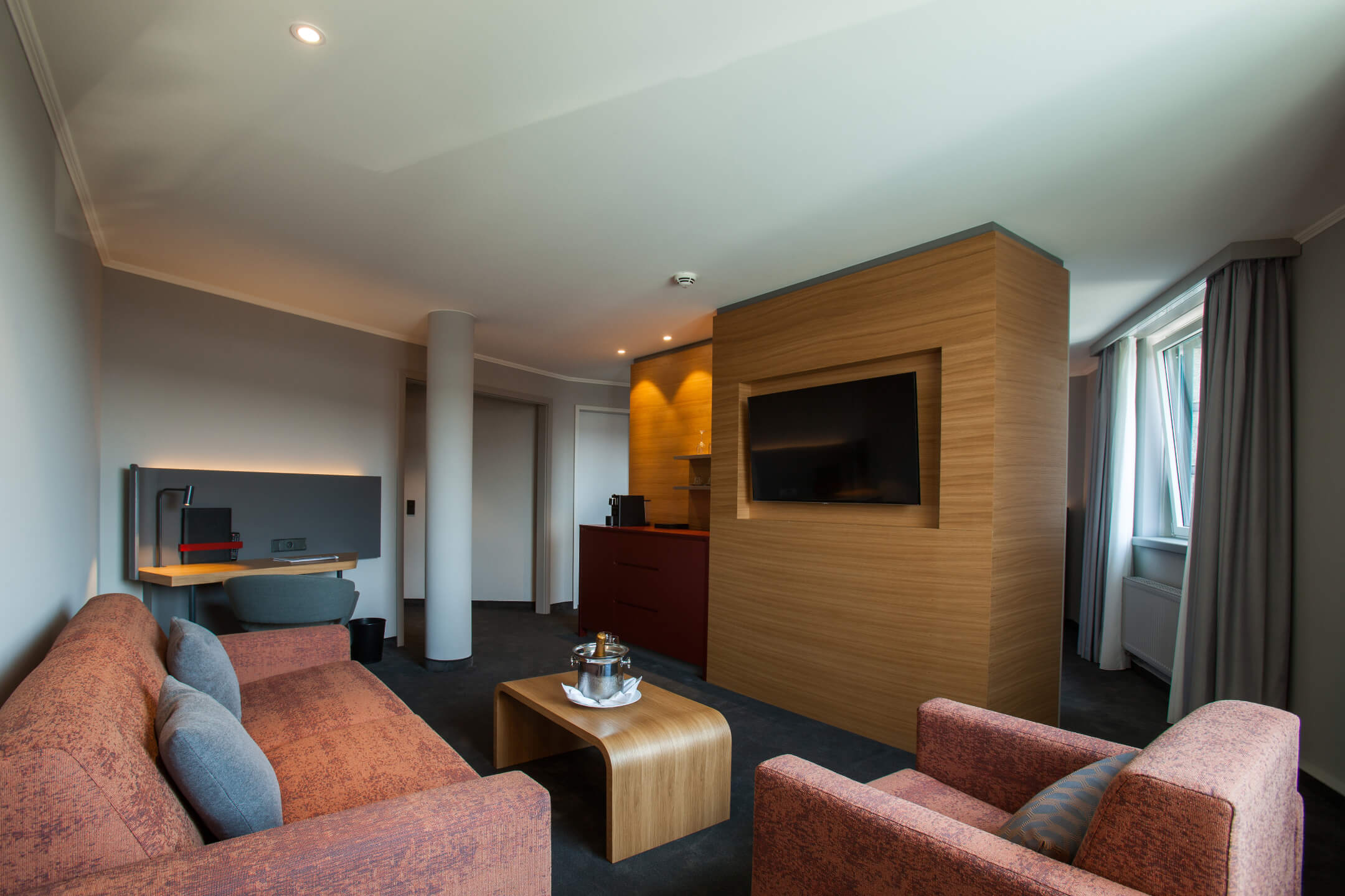 Modernes Hotelzimmer mit gemütlicher Sitzecke, Flachbild-TV, Schreibtisch und großem Fenster.