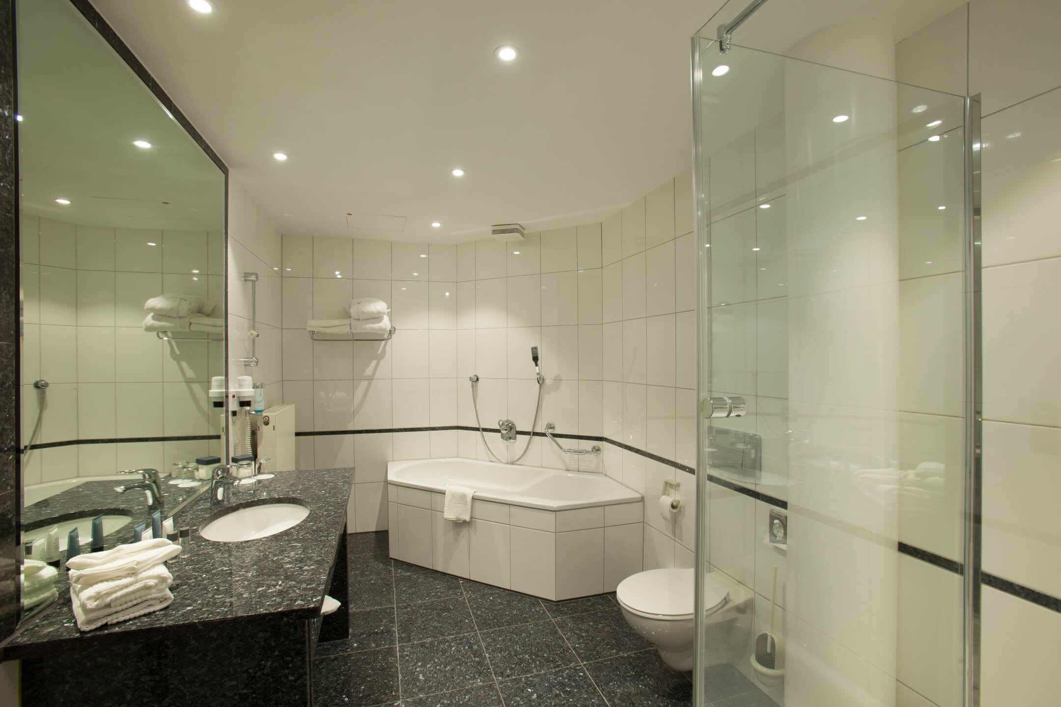 Modernes Badezimmer mit großer Badewanne, Dusche, Doppelwaschbecken und weißen Fliesen im ATLANTIC Hotel Airport Bremen.