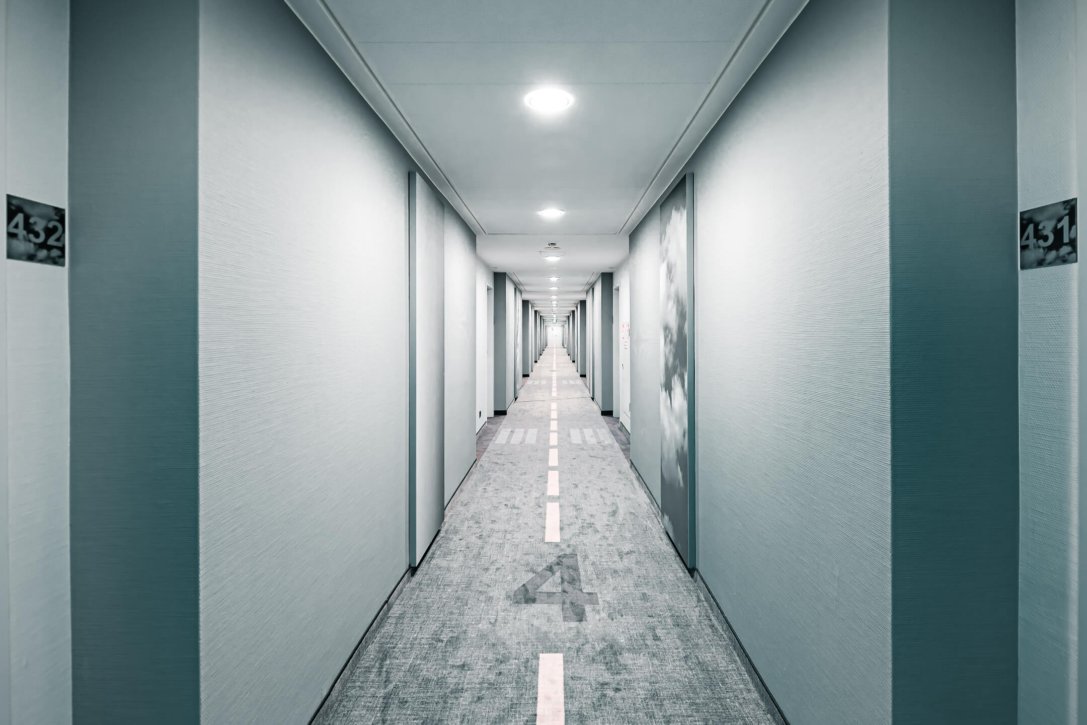 Heller Hotelgang mit Teppichboden, der eine Landebahn imitiert, Türen zu den Zimmern auf beiden Seiten.