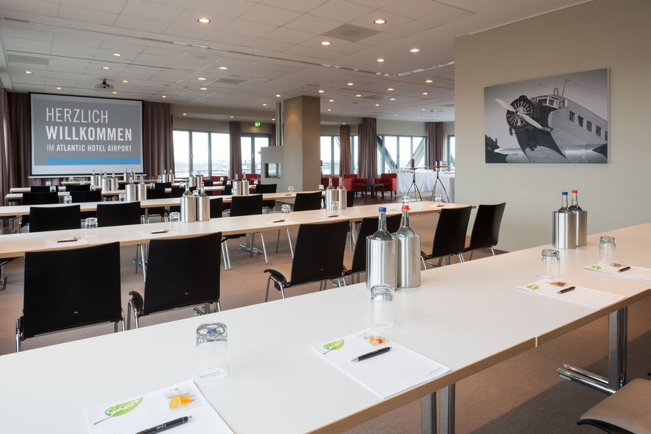Heller Konferenzraum im ATLANTIC Hotel Airport Bremen mit Tischen, Stühlen und Willkommensschild.