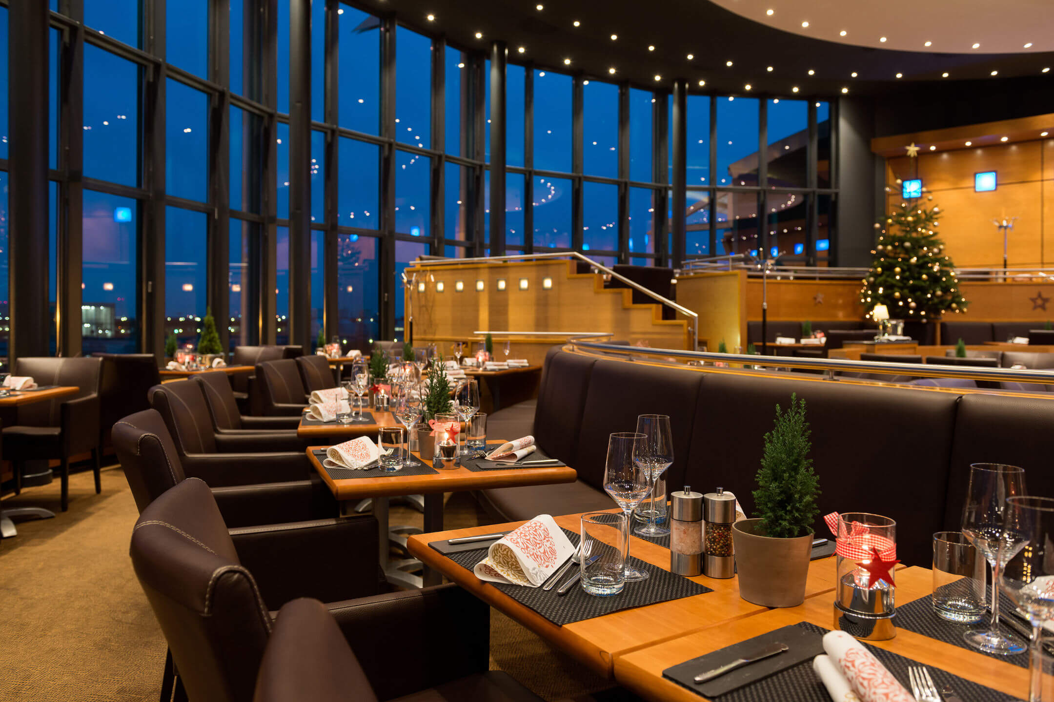 Elegantes Restaurant im ATLANTIC Hotel Airport Bremen, festlich gedeckt mit Kerzen, großem Fenster und Weihnachtsbaum.