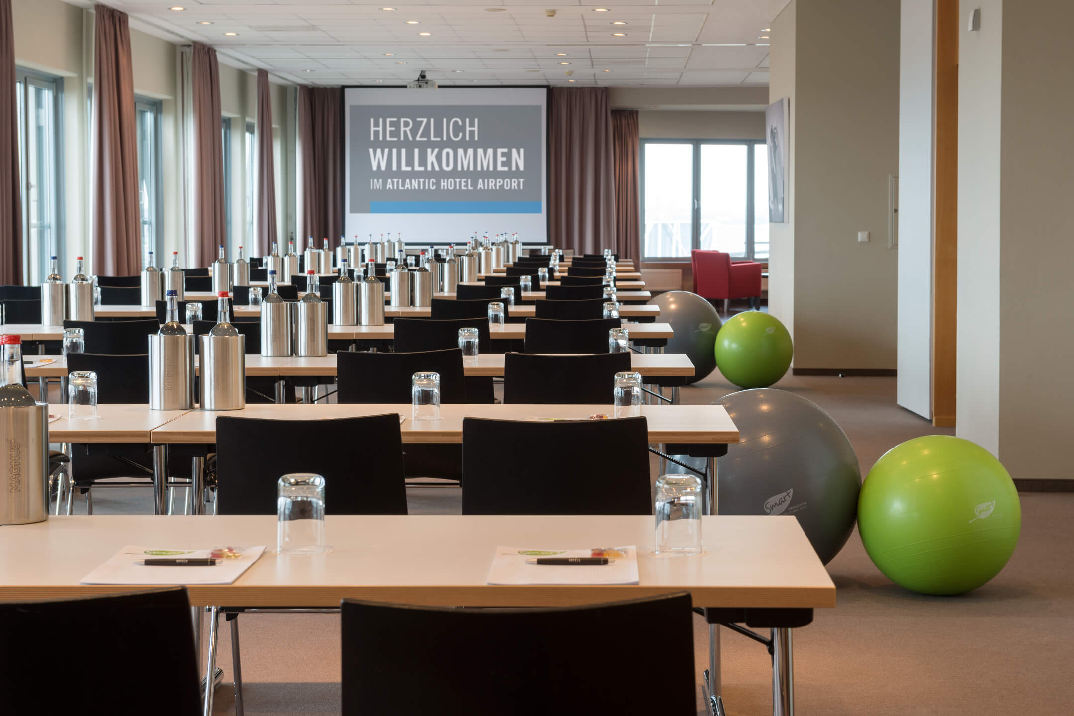 Konferenzraum im ATLANTIC Hotel Airport Bremen, mit Tischen, Stühlen, Getränken und Gymnastikbällen, Begrüßungsbanner im Hintergrund.