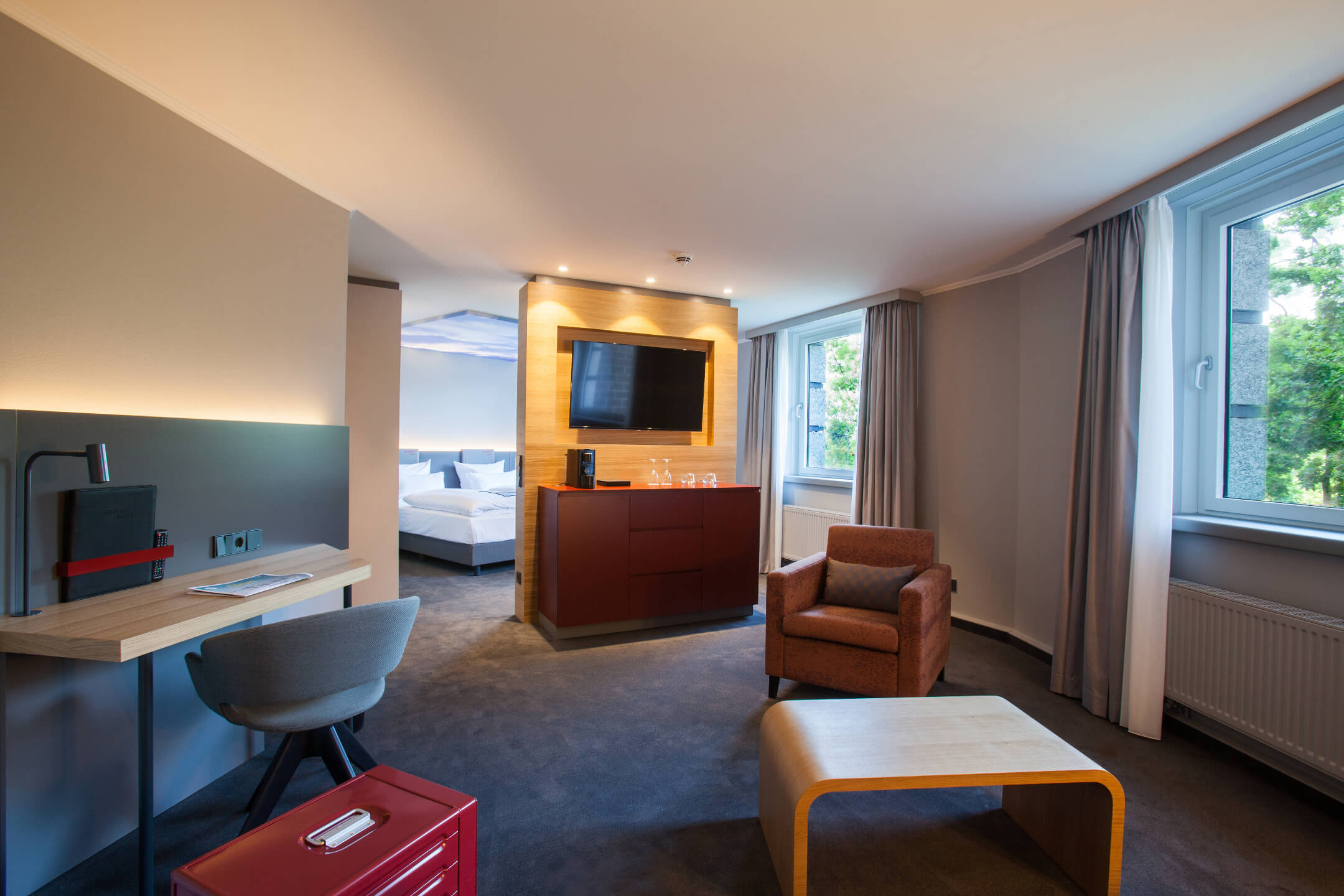 Modern hotel room with seating area, desk, TV, large window and view of the bedroom at the ATLANTIC Hotel Airport.