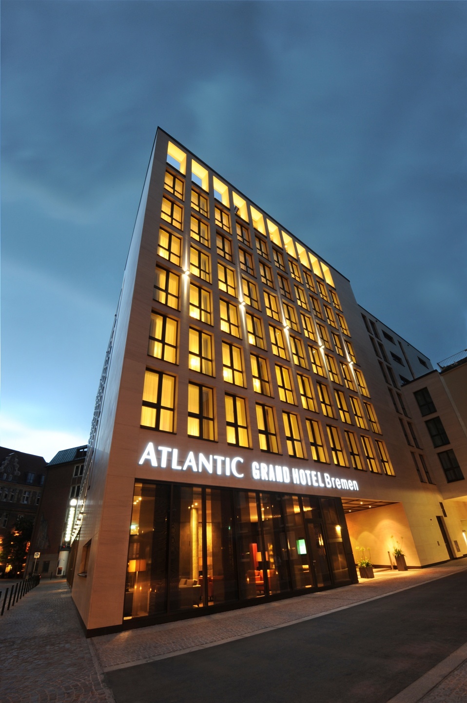 Modern hotel building at dusk, with illuminated windows and the lettering "ATLANTIC Grand Hotel Bremen".