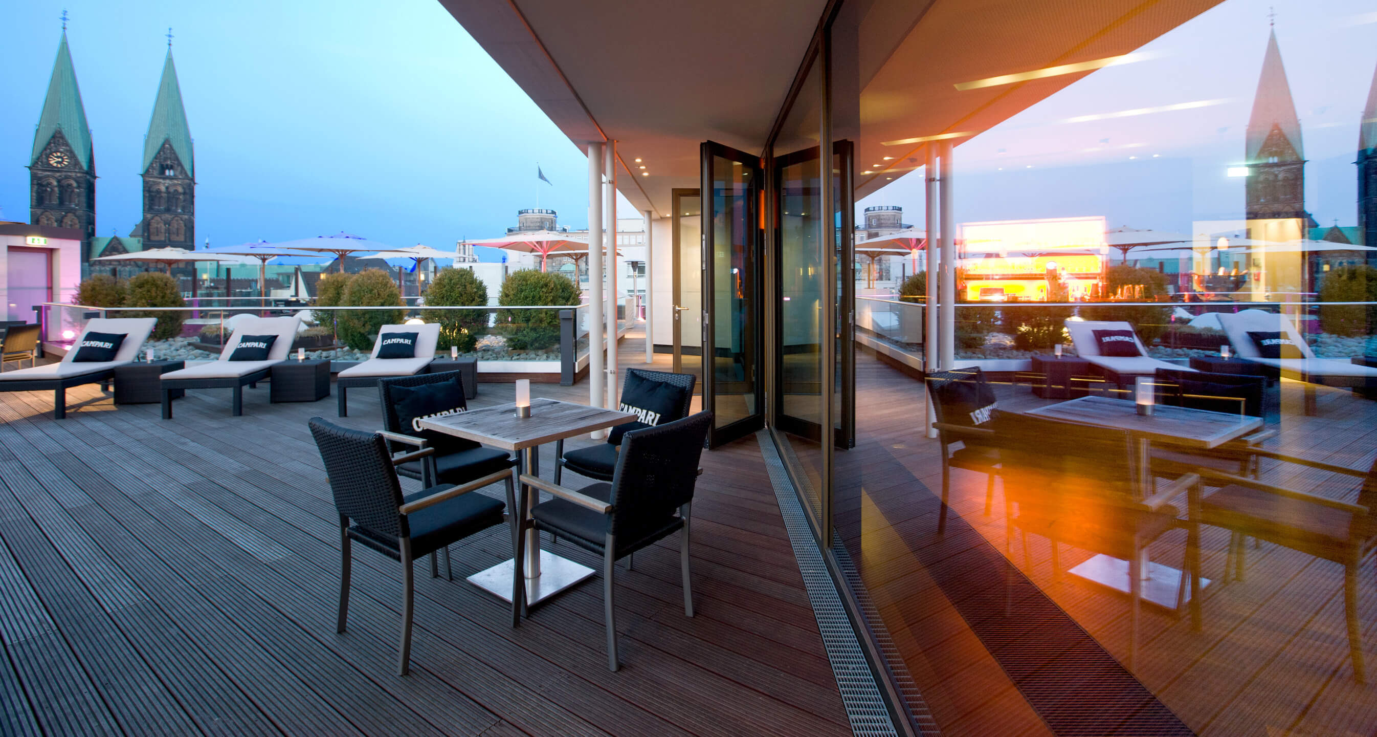 Modern hotel terrace with seating, view of Bremen's cathedral towers in the background.