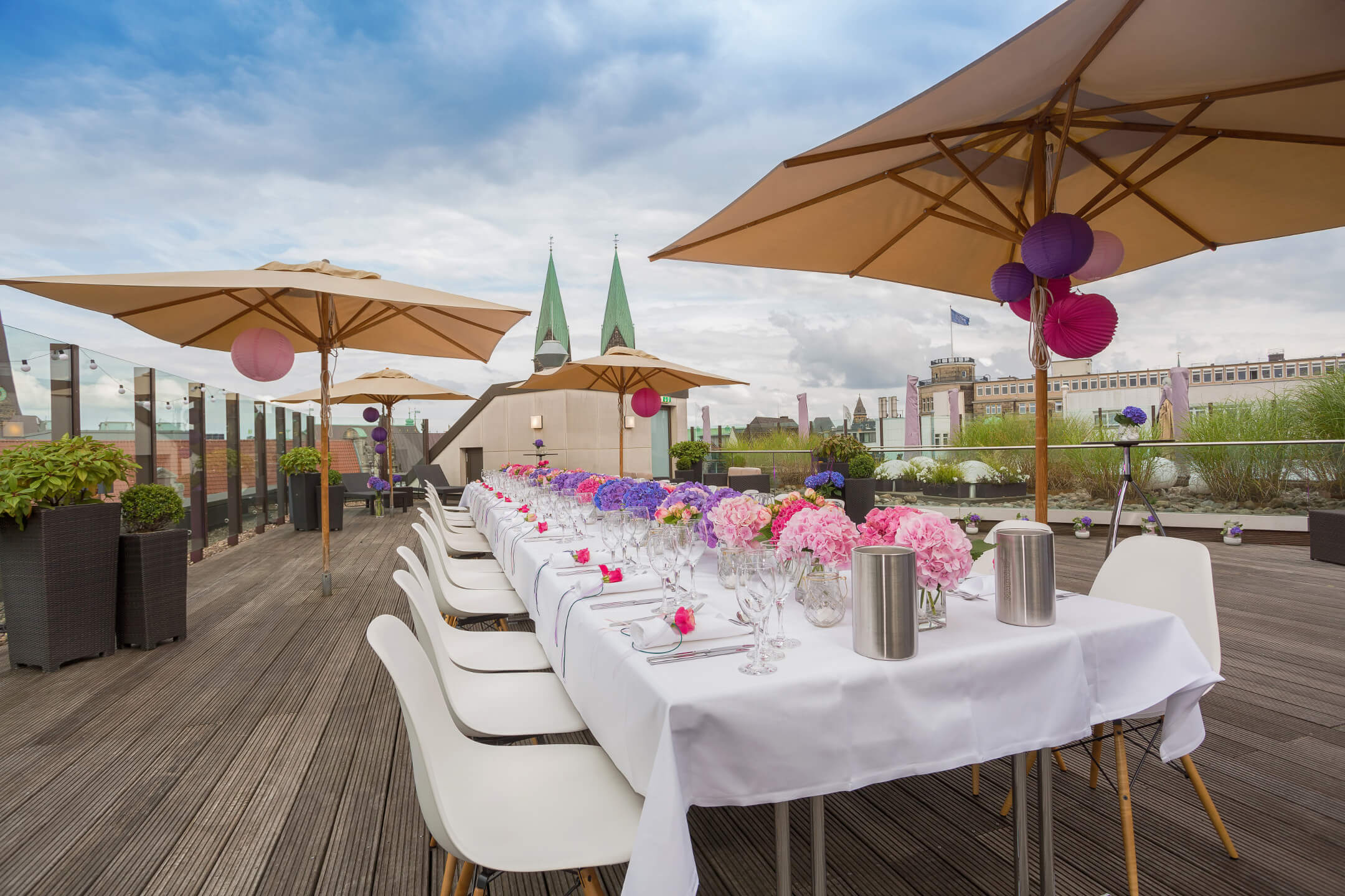 Festively laid table on the roof terrace of the ATLANTIC Grand Hotel Bremen with flowers and parasols.