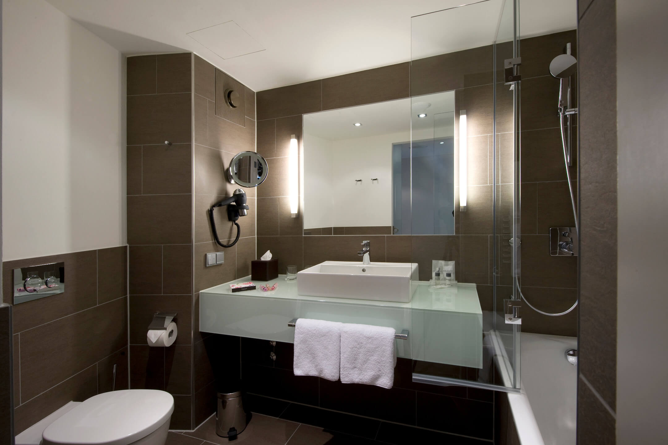 Modern hotel bathroom with glass washbasin, illuminated mirror, bathtub and towel rail at the ATLANTIC Grand Hotel Bremen.