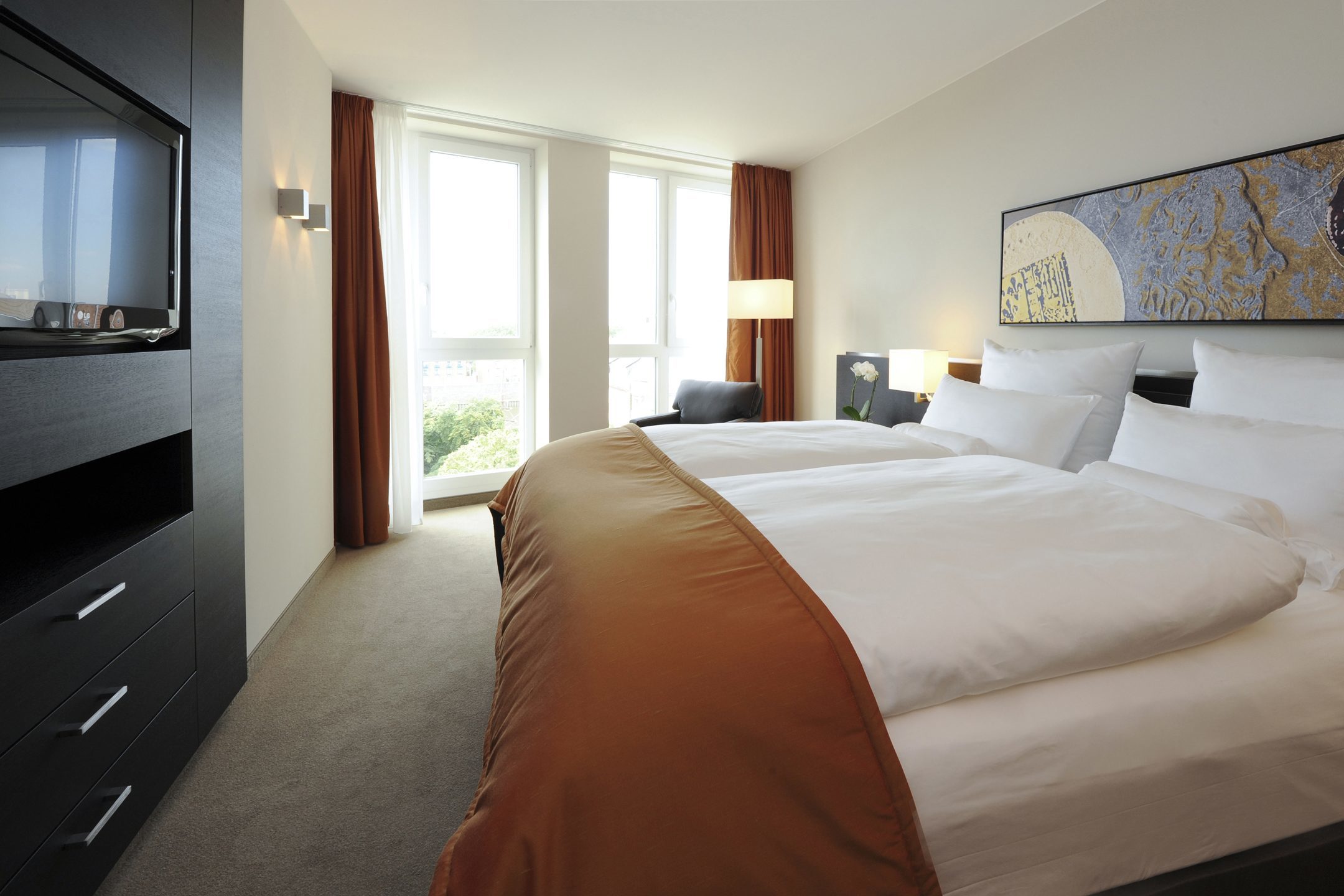 Bright hotel room with double bed, modern furnishings, large window and artwork on the wall at the ATLANTIC Grand Hotel Bremen.