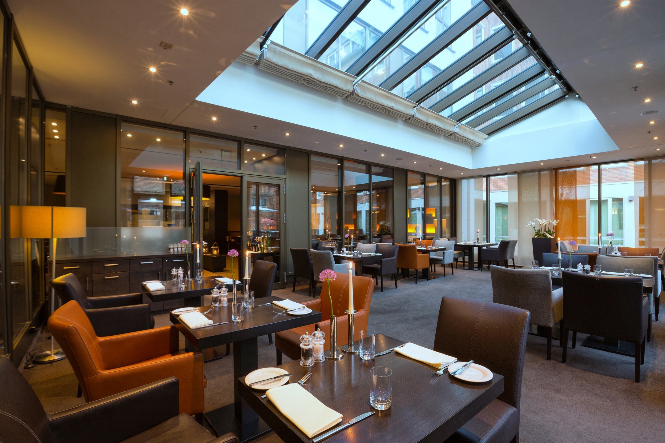 Modern hotel restaurant with glass roof, elegant tables and cozy armchairs at the ATLANTIC Grand Hotel Bremen.