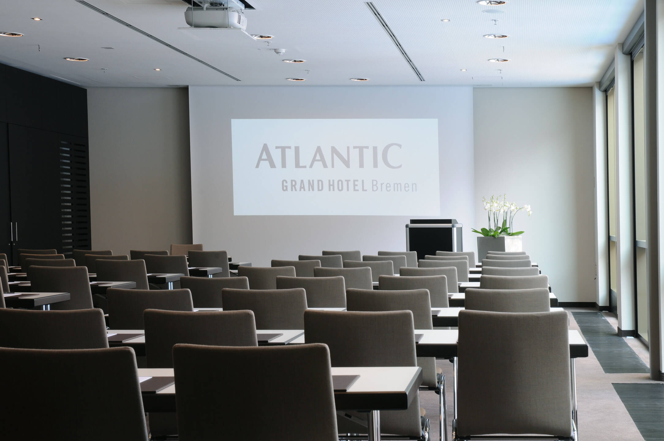 Modern conference room in the ATLANTIC Grand Hotel Bremen with rows of chairs, screen and lectern.