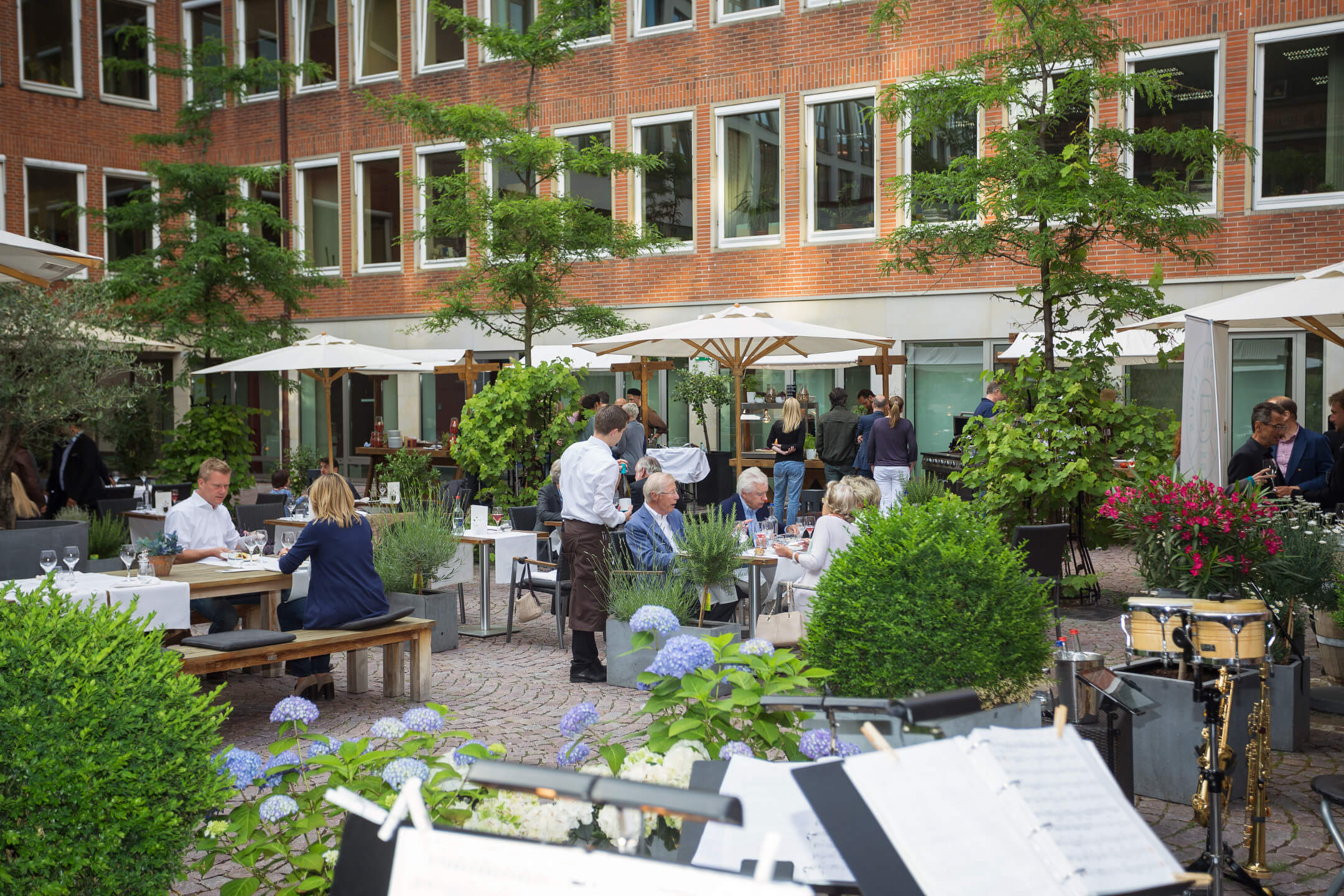 Garden restaurant of the ATLANTIC Grand Hotel Bremen with guests at tables, surrounded by plants and parasols.
