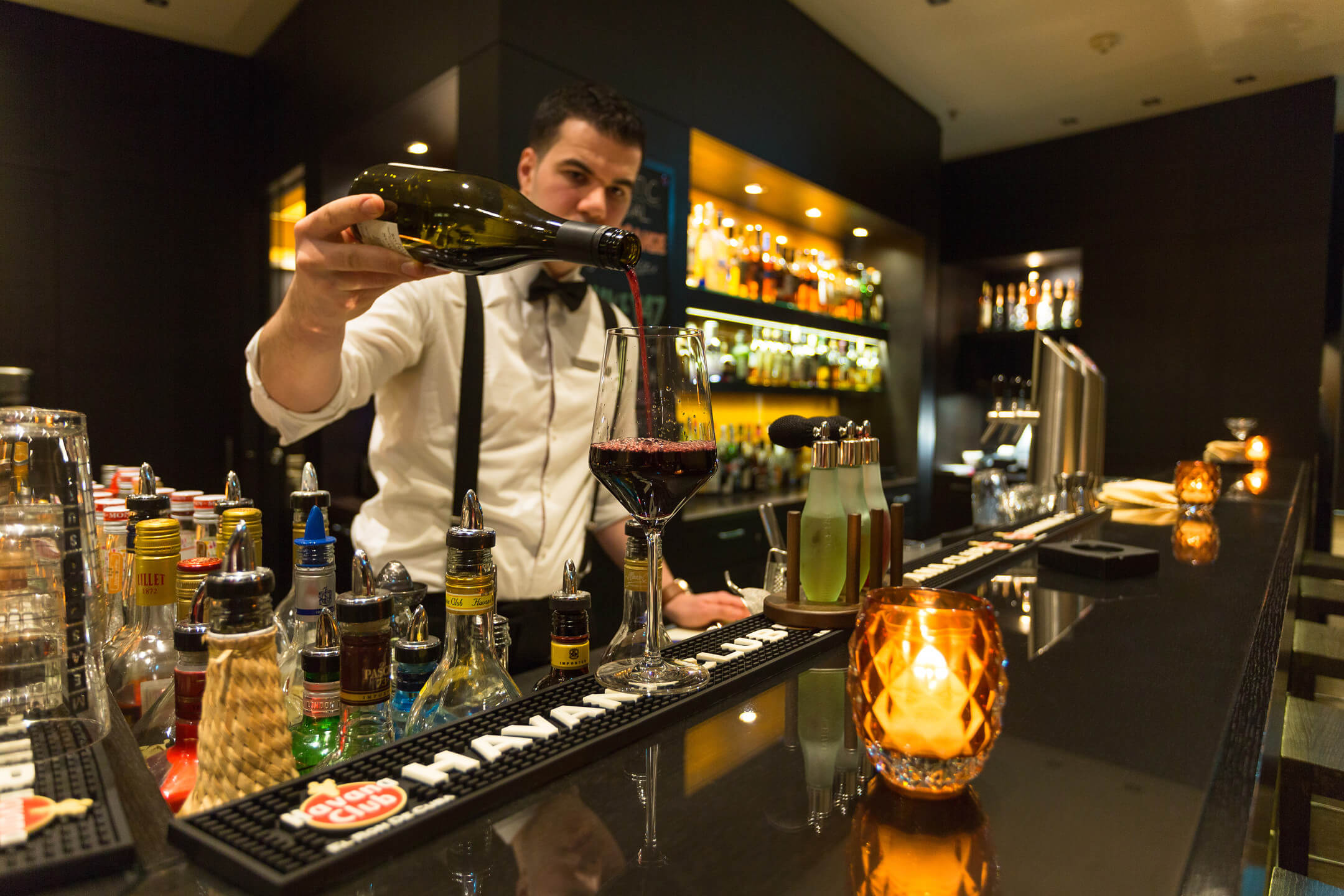 Bartender at the ATLANTIC Grand Hotel Bremen pours red wine in a stylish bar with cozy lighting.