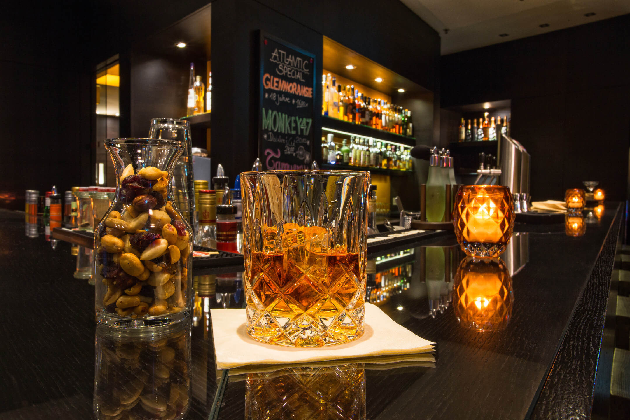 Cozy hotel bar with drinks, nuts and candlelight on a dark counter.