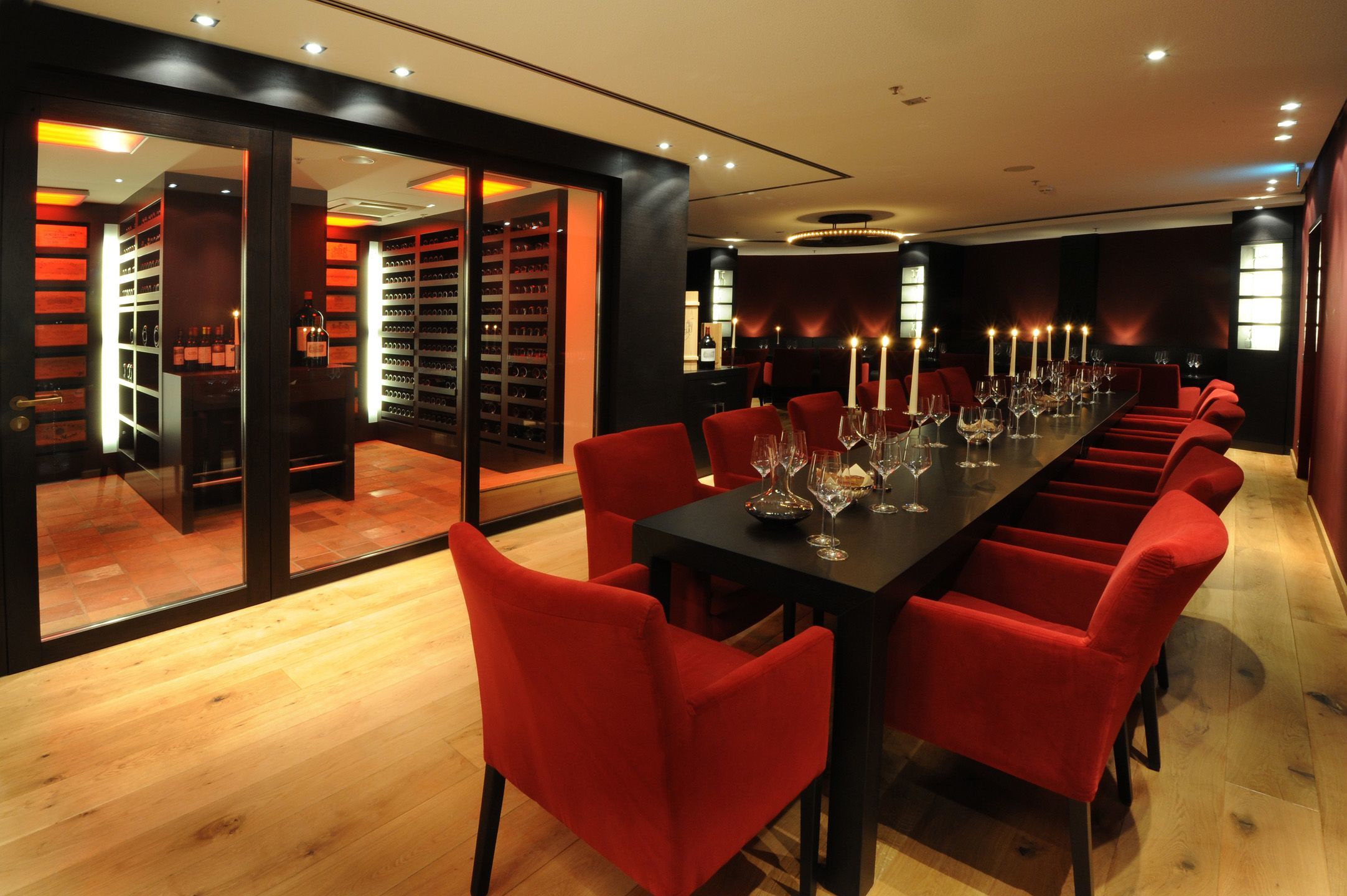 Elegant hotel wine room with red decor, long table, red chairs and candlelight.