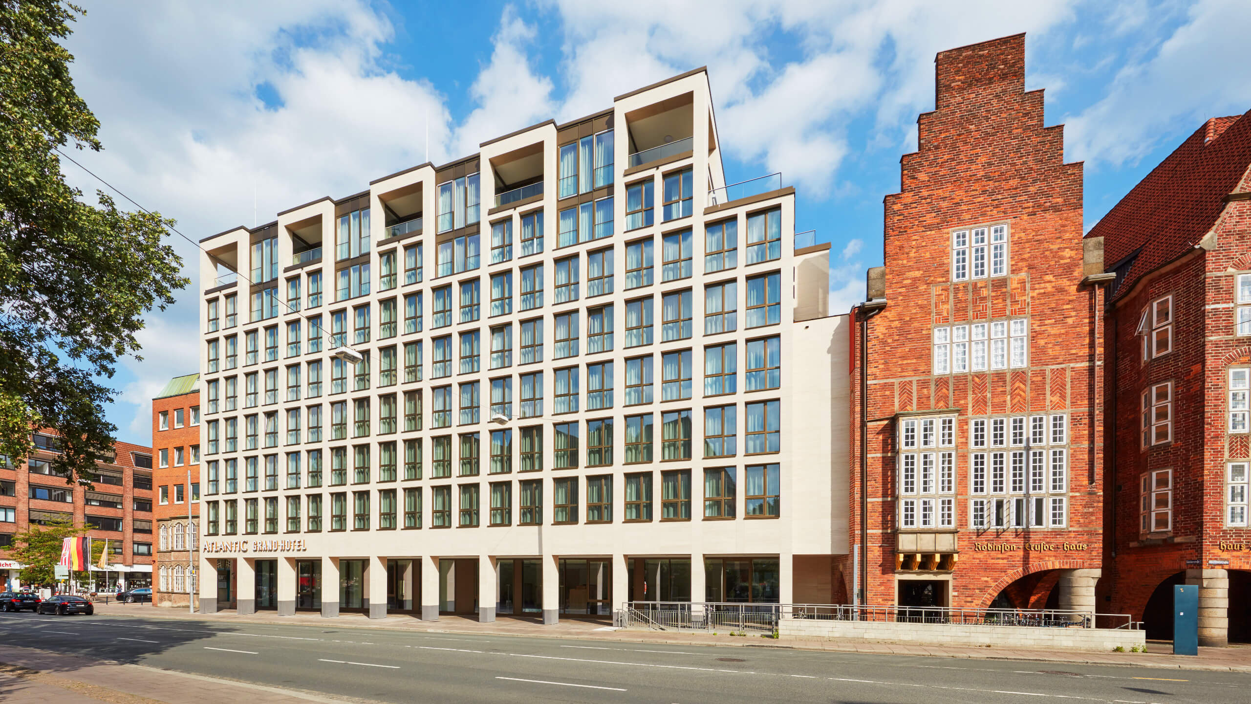 Facade of the ATLANTIC Grand Hotel Bremen, modern building next to a historic brick house under a blue sky.