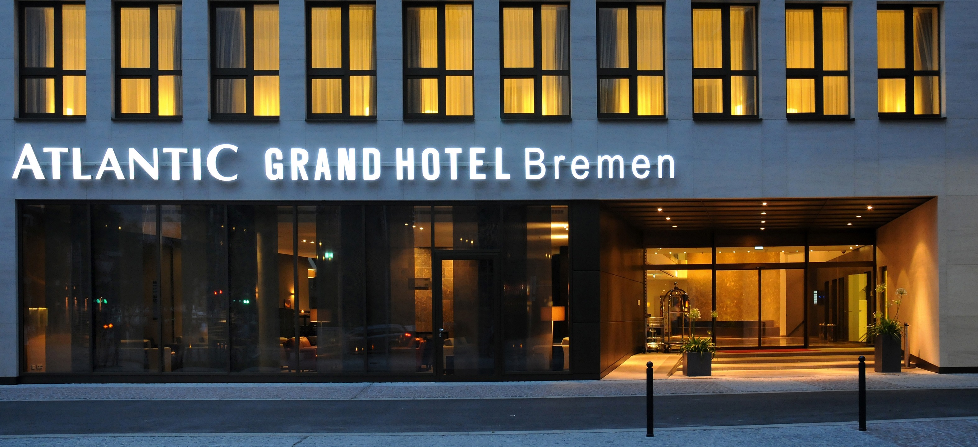 Entrance to the ATLANTIC Grand Hotel Bremen at night with illuminated lettering and glass façade.