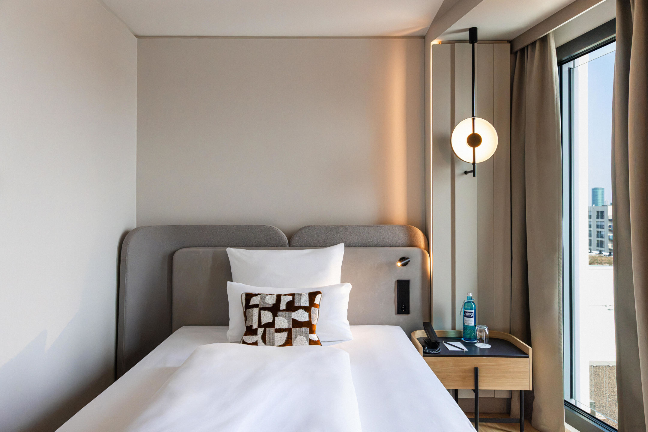 A modern single bed and bedside table with a bottle of water.