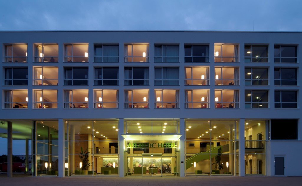 Moderne Hotel-Fassade bei Dämmerung, beleuchtete Fenster und Eingang des ATLANTIC Hotel Galopprennbahn in Bremen.