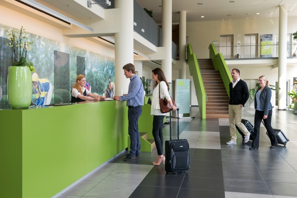 Hotelrezeption mit grüner Theke, Gäste beim Einchecken, Treppe im Hintergrund.