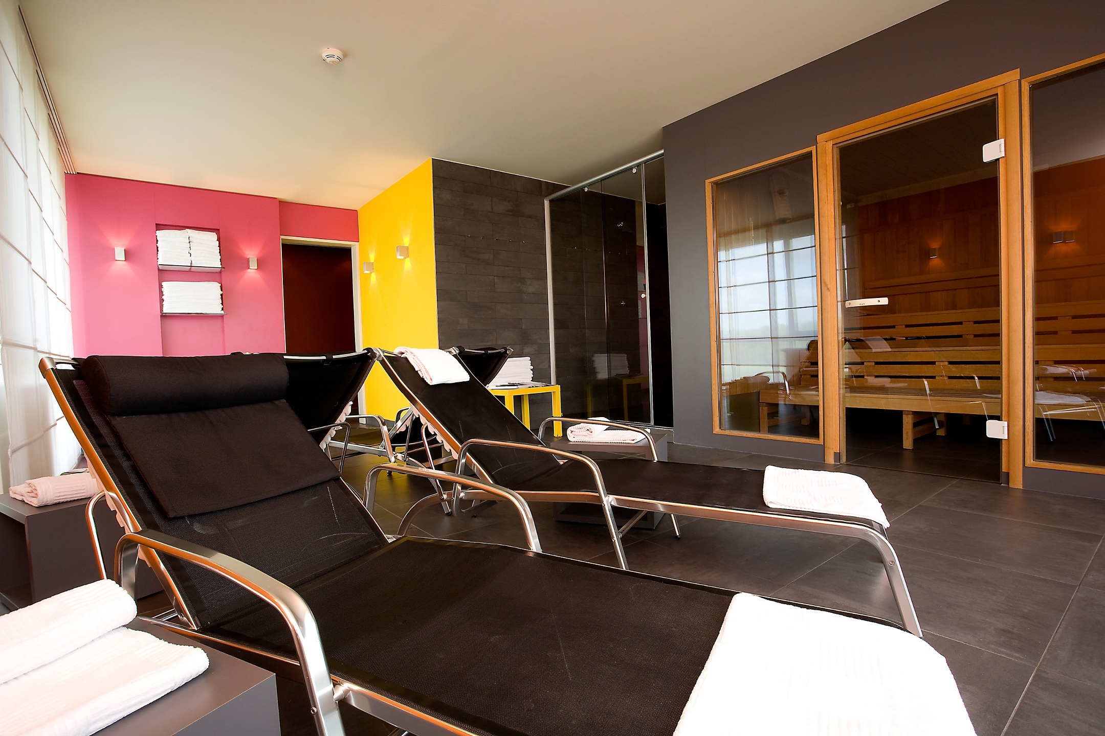 Moderner Wellnessbereich mit Liegestühlen, Sauna und farbigen Wänden im ATLANTIC Hotel Galopprennbahn, Bremen.