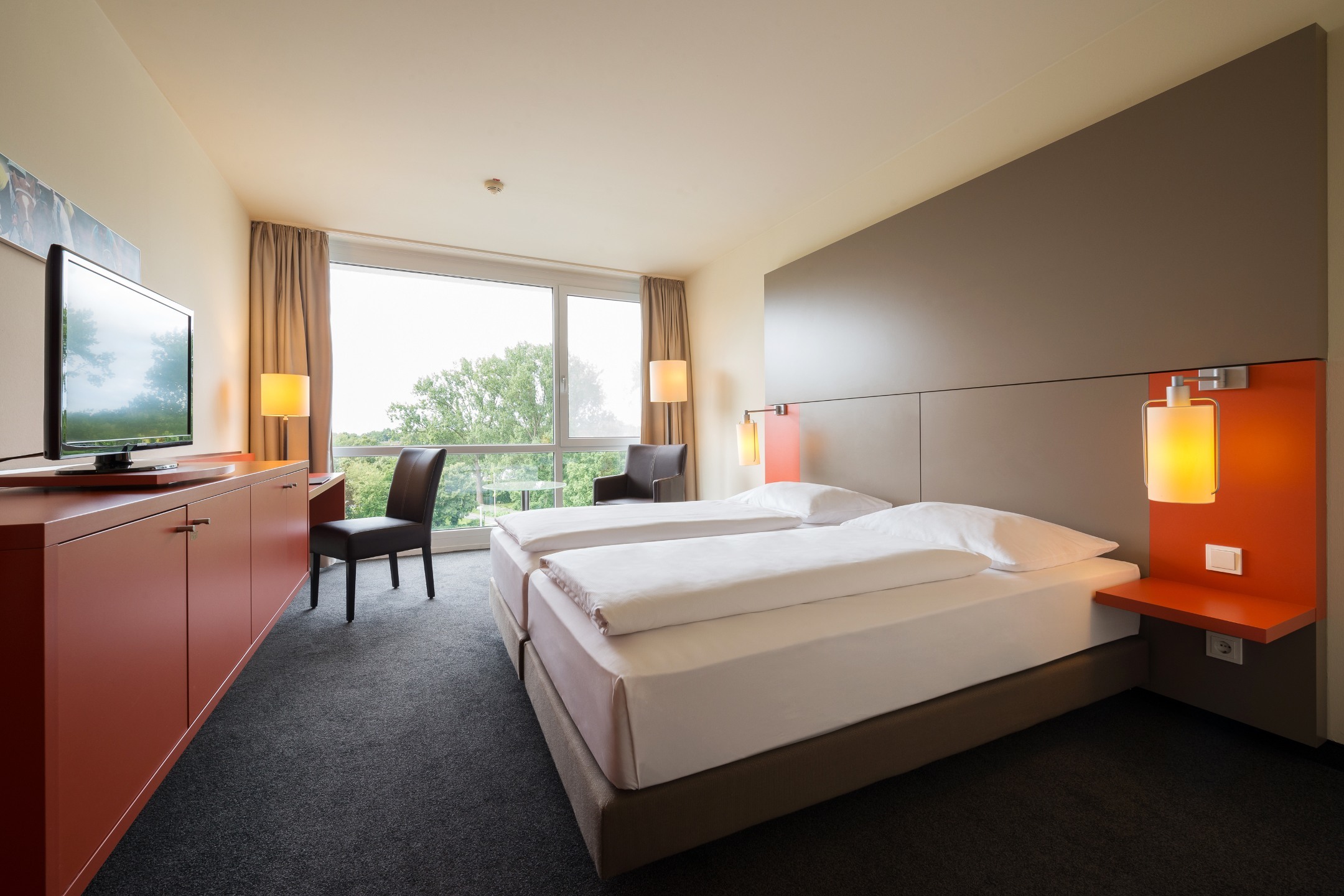 Bright hotel room with double bed, large window, TV, desk and modern furnishings at the ATLANTIC Hotel Galopprennbahn.