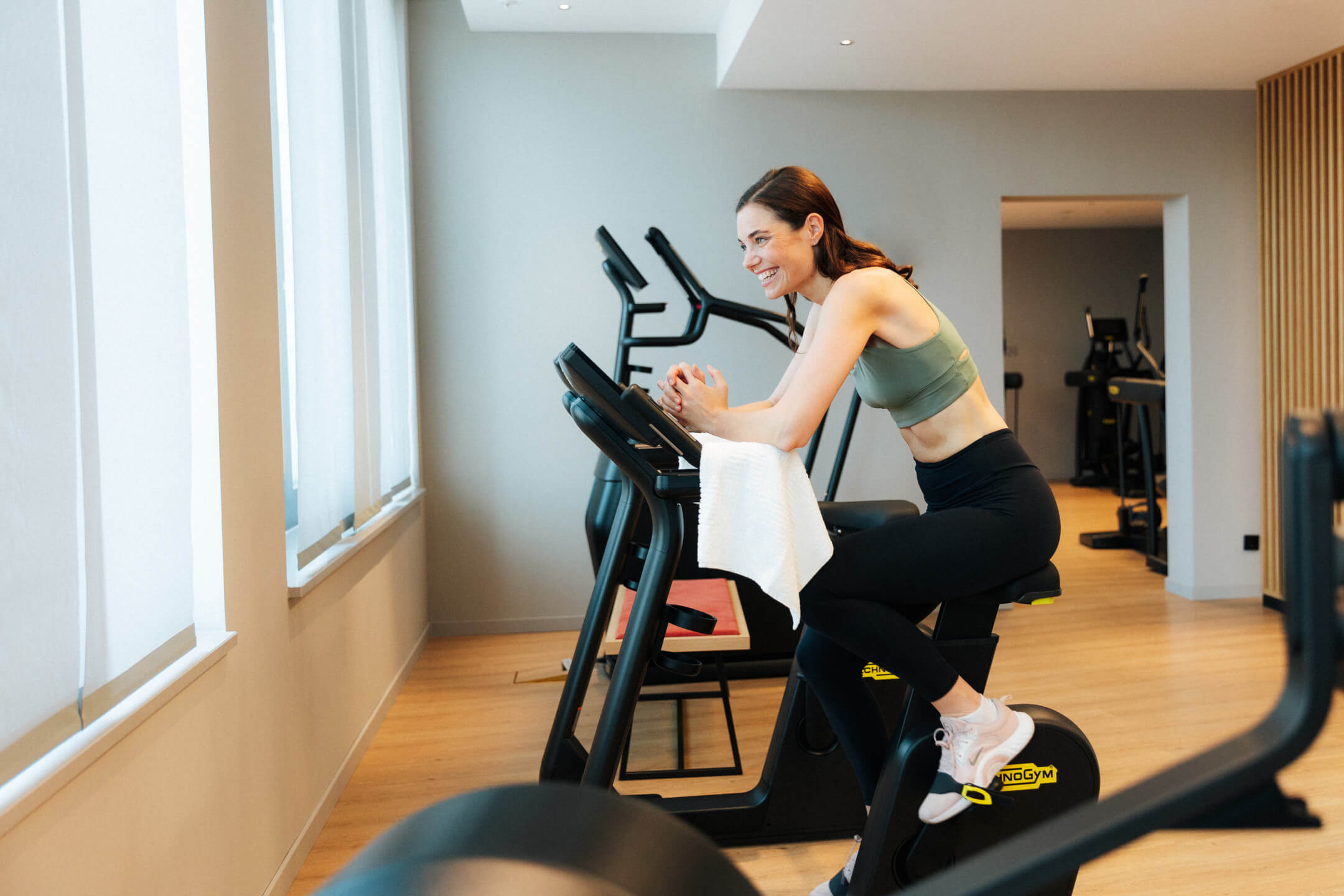 ATLANTIC Hotel Heidelberg Fitness Frau trainiert auf einem Fitnessbike im lichtdurchfluteten Fitnessraum des ATLANTIC Hotel Heidelberg.
