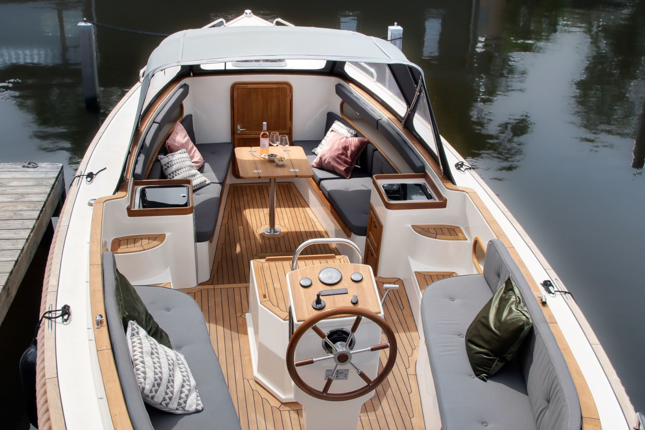Luxurious motorboat with comfortable seating, table and steering wheel, docked on the water.