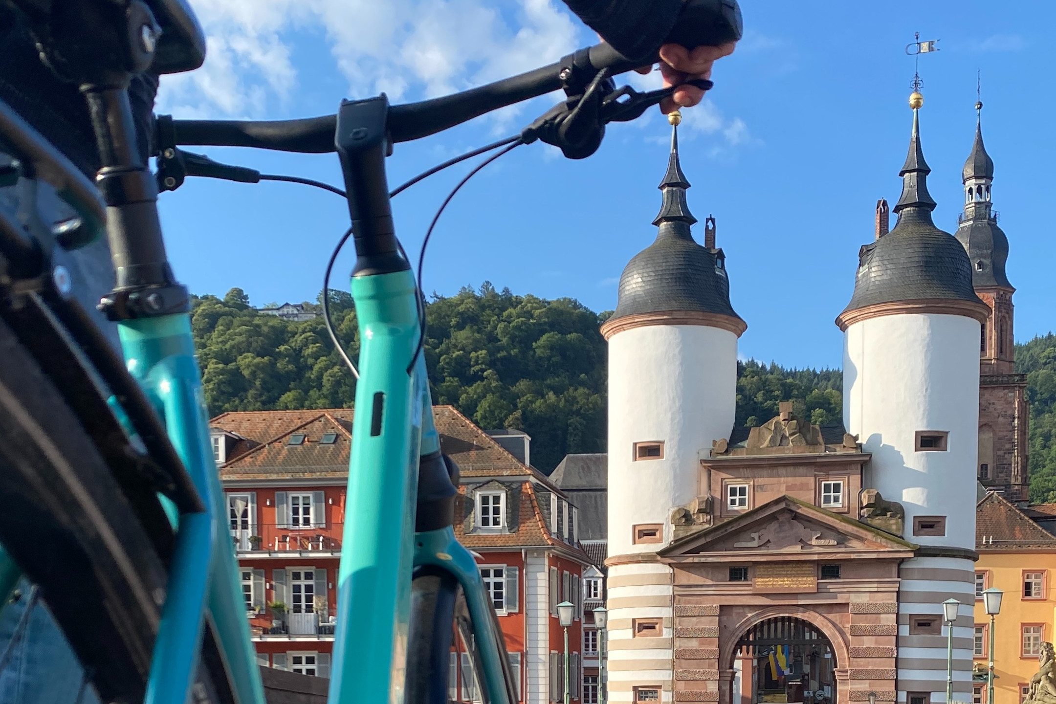 Bicycle in front of historic city gate in Heidelberg with green landscape and blue sky in the background.