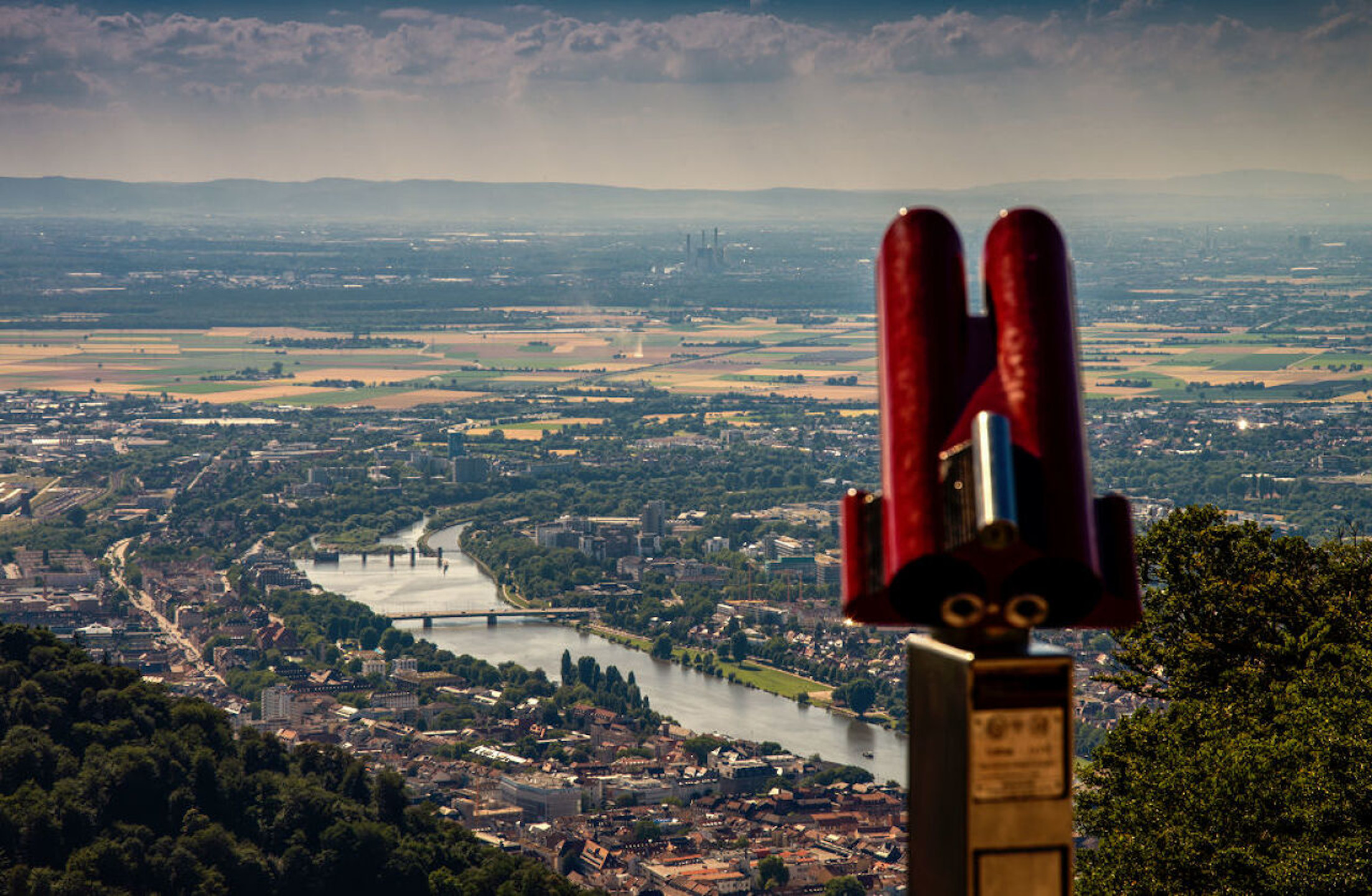 View of a town with a river and fields, in the foreground a pair of red binoculars on a vantage point.