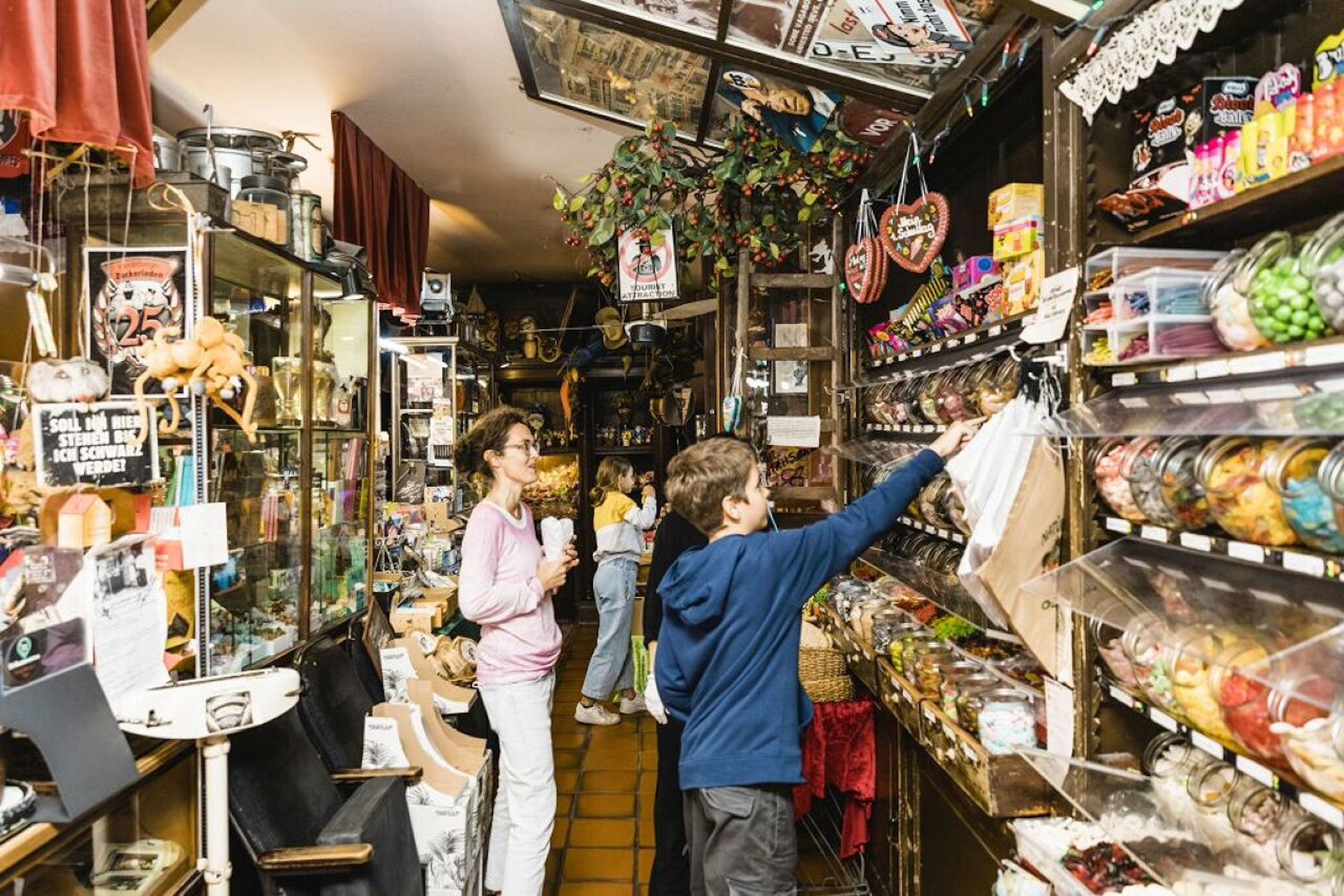 A small, colorful candy store with shelves full of sweets where people browse and choose.