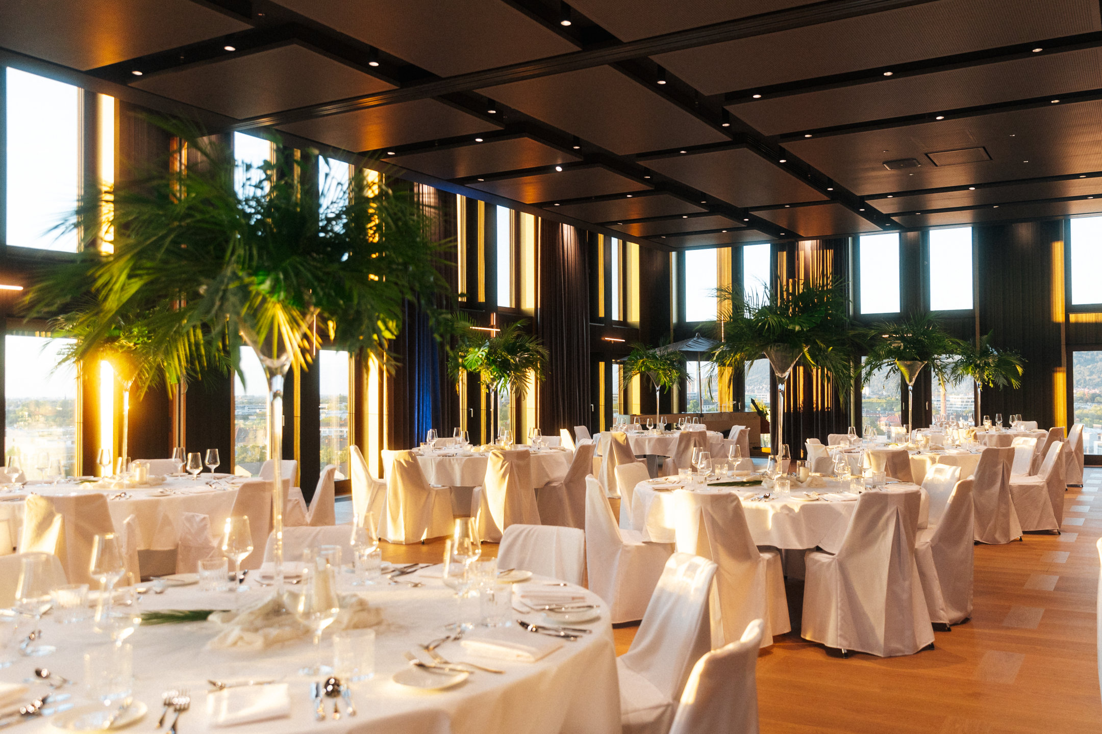 Der Ballsaal in goldener Abendsonne, mit runden Tischen auf denen weiße Tischdecken und ein festliches Gedeck sind.