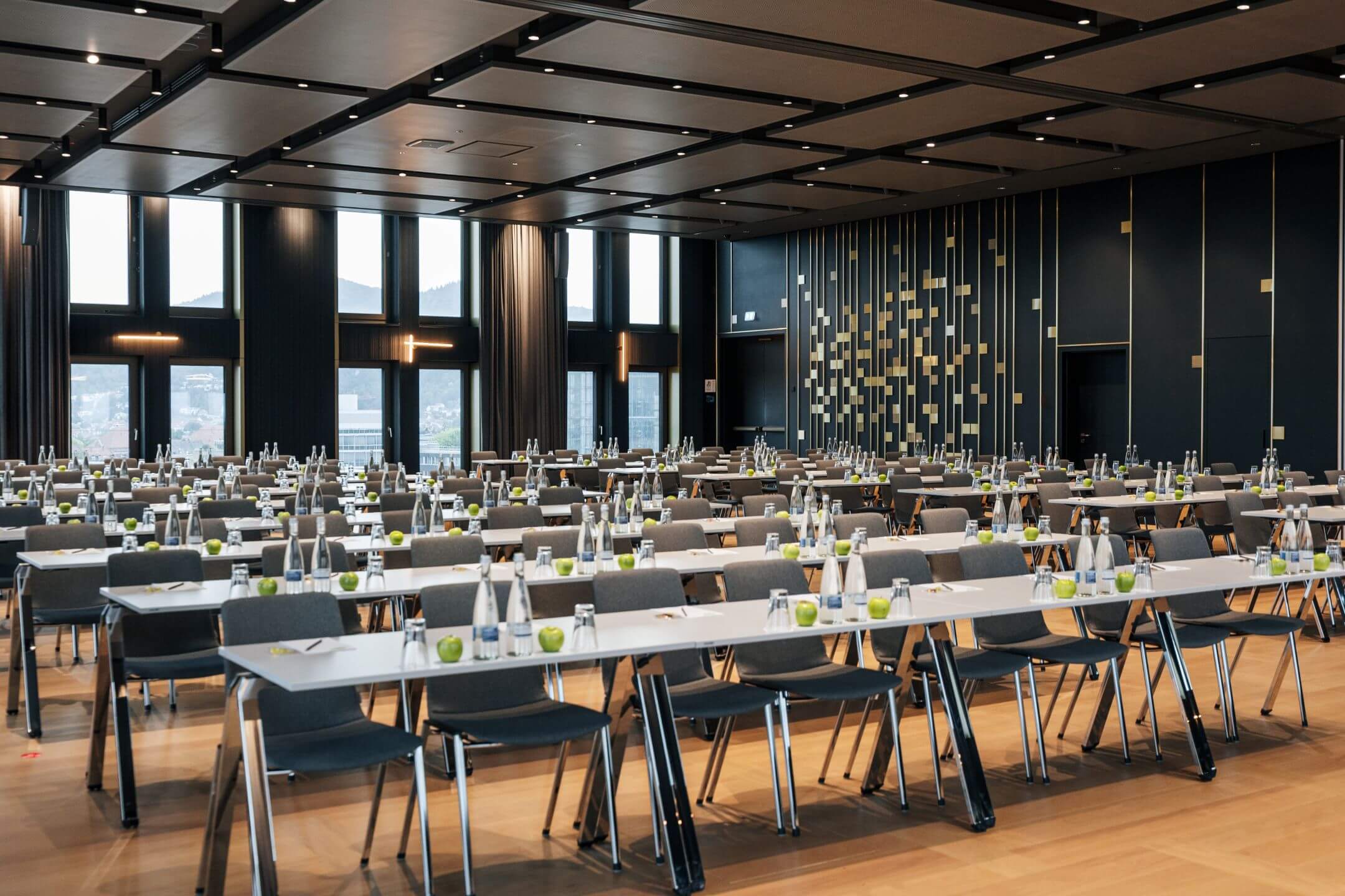 Moderner Konferenzraum im ATLANTIC Hotel Heidelberg mit Reihen von Tischen und Stühlen, großen Fenstern und eleganter Beleuchtung.