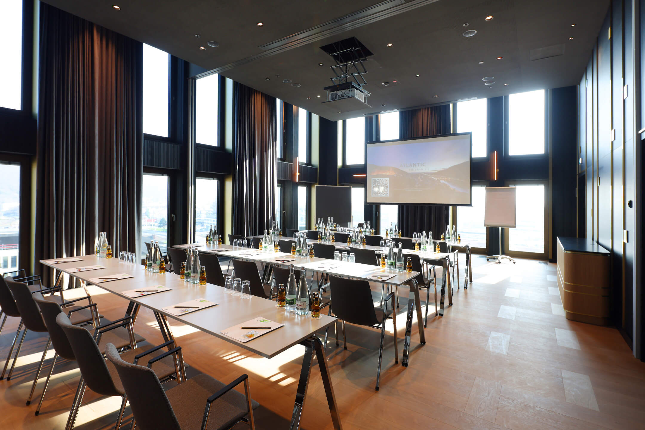 Saal 1 im ATLANTIC Hotel Heidelberg, Eckraum mit zwei Fensterfronten, parlamentarisch bestuhlt und Tische eingedeckt mit Schreibblöcken und Getränken