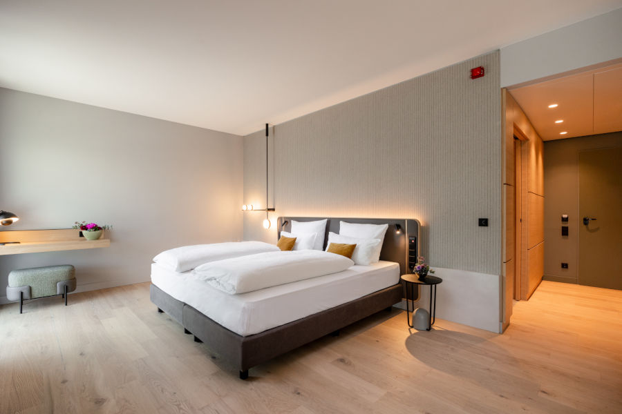 Modern hotel room with double bed, wooden floor, desk, plants and subtle lighting at the ATLANTIC Hotel Heidelberg.