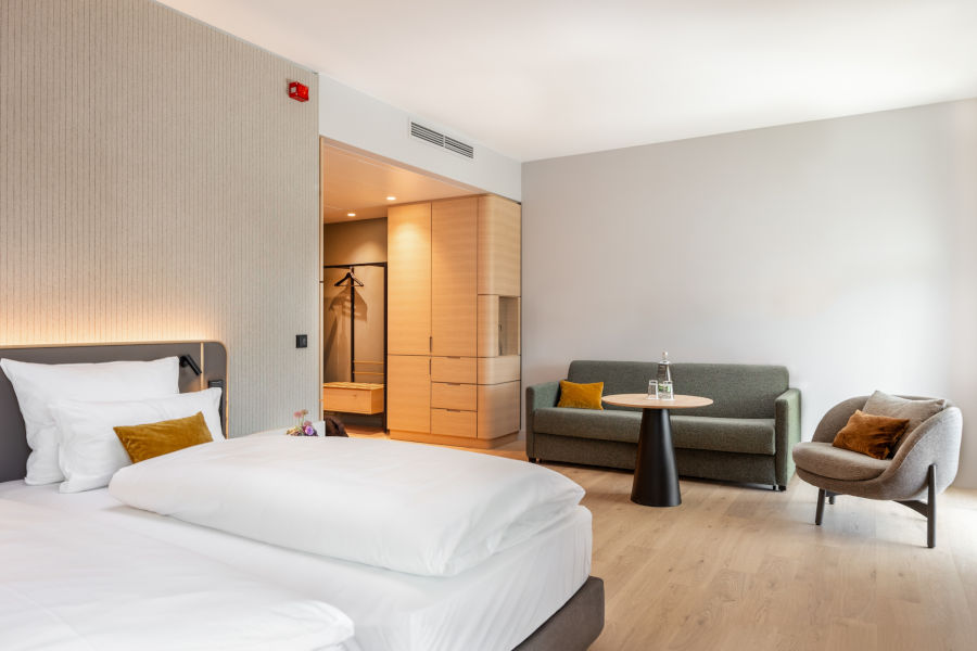 Modern hotel room with double bed, sofa, armchair and table, light colors, minimalist design at the ATLANTIC Hotel Heidelberg.