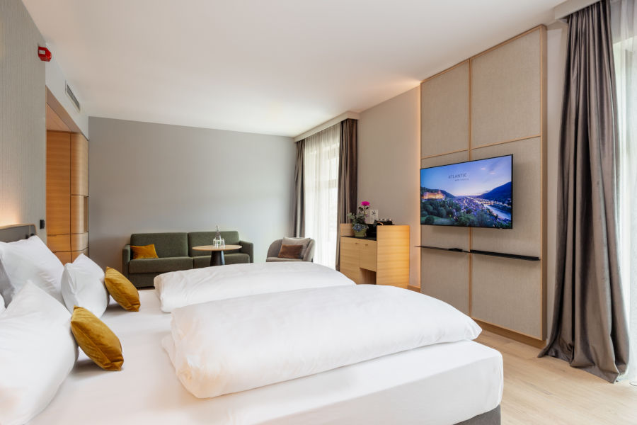 Modernes Hotelzimmer mit Doppelbett, Sofa, Flachbild-TV und großen Fenstern im ATLANTIC Hotel Heidelberg.