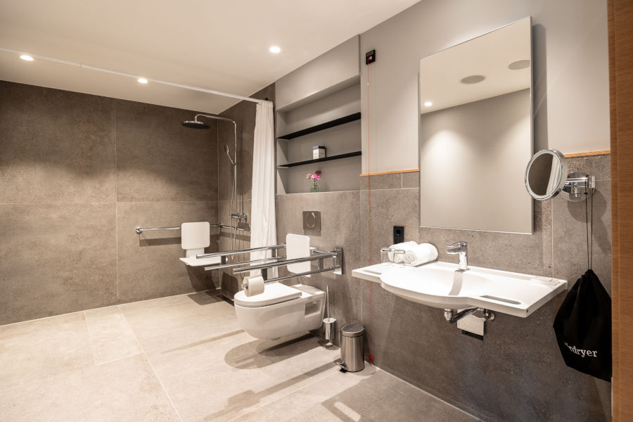 Barrier-free bathroom in the ATLANTIC Hotel Heidelberg with shower, WC and washbasin, equipped with grab rails.