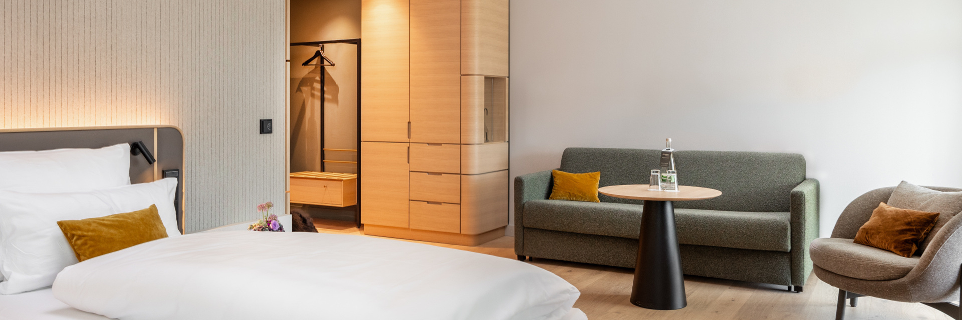 Blick auf das gemachte Bett und die Sitzecke mit Sofa und Sessel im barrierearmen Zimmer