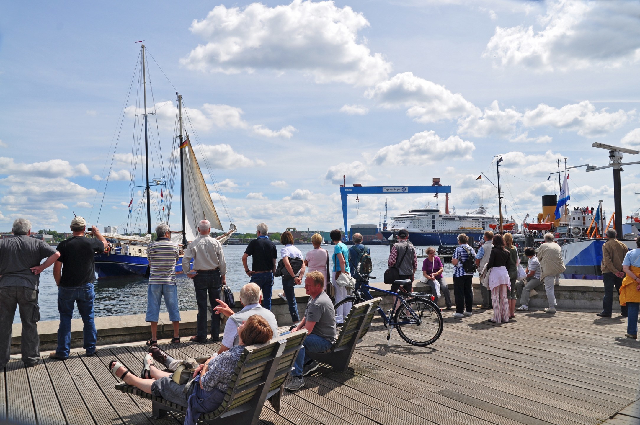 Besucher an der Förde Kiels Menschen beobachten Segelboote und ein Kreuzfahrtschiff am Kieler Hafen bei sonnigem Wetter.